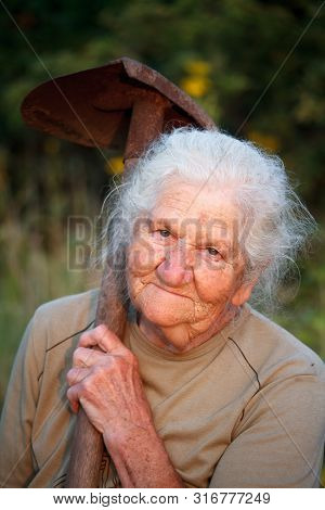 Close-up Portrait Of An Old Woman With Gray Hair Smiling And Looking At The Camera, Holding A Rusty