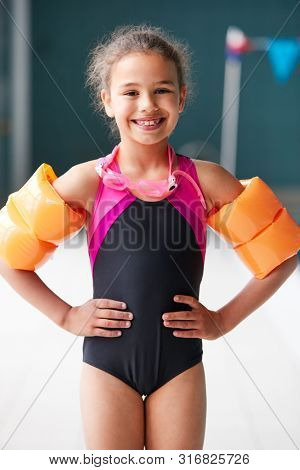 Portrait Of Girl Wearing Armbands Standing By Edge Of Swimming Pool Ready For Lesson