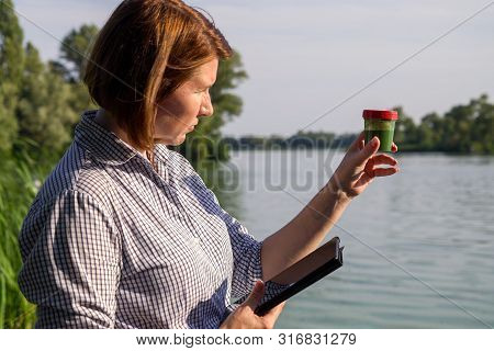 Side View Of Researcher With Tablet Examines Tube With Green Algae Outside
