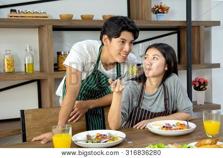 Cute Happy Couple In Aporn Having Breakfast Having Salad In Modern Kitchen And Having A Good Time