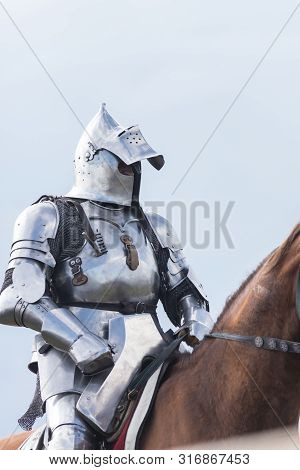 A Man Knight With Half Opened Helmet Riding A Brown Horse Holding A Sword