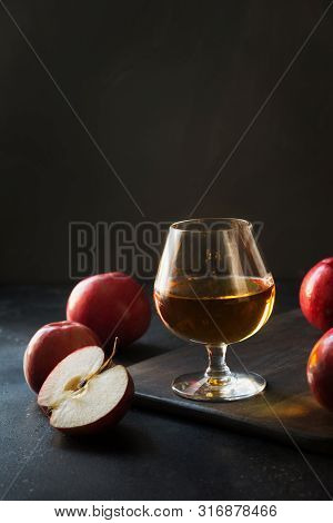 Glass With Calvados Brandy And Red Apples On Black.