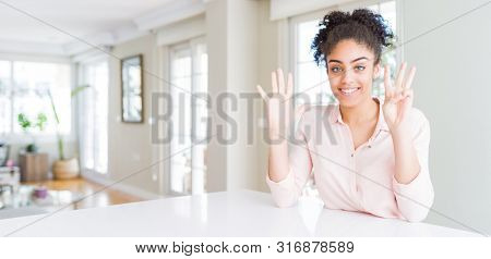 Wide angle of beautiful african american woman with afro hair showing and pointing up with fingers number eight while smiling confident and happy.