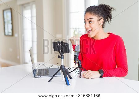 Young african american woman doing video call using smartphone camera and microphone smiling with happy face looking and pointing to the side with thumb up.