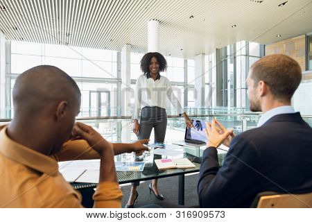 Over shoulder view of young African American businesswoman standing to make a presentation to two African American and Caucasian male colleague. Modern corporate start up new business concept with