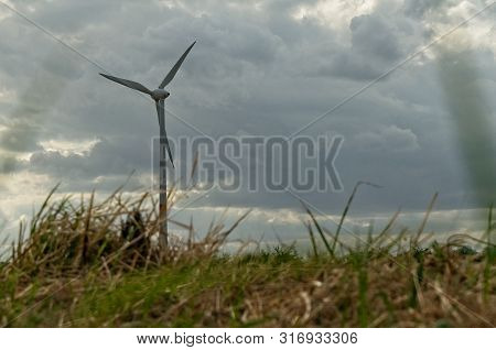 Wind Turbine Behind Blurred Straws Under A Cloudy Sky