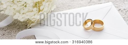 Panoramic Shot Of Golden Rings On Envelope Near White Ribbon And Hortense Flower On Grey Textured Su