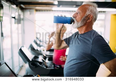 Senior Man Drinking Bottle Of Water On Threadmill In Gym