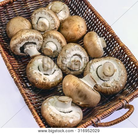 A Collection Of Cremini Mushrooms In A Basket Placed On A White Background.