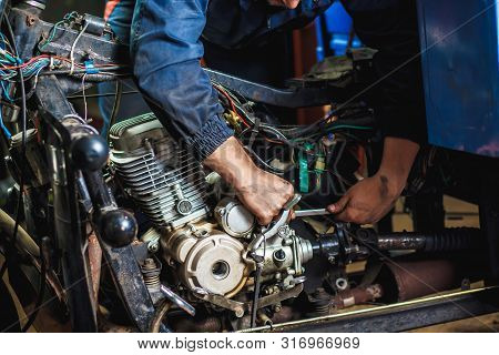 Specialist In Coveralls Working With Motorized Bicycles At Repair Garage. Hands In The Frame. Close-