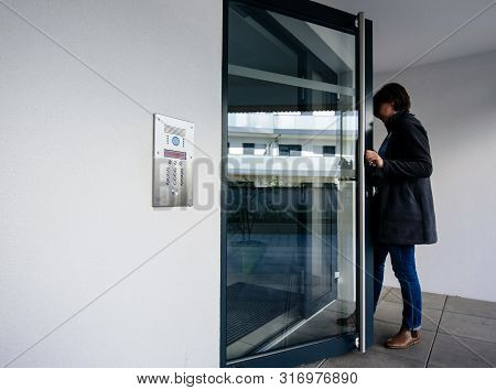 Side View Of Woman Entering Modern Apartment Building With Glass Door And Modern Intercom System