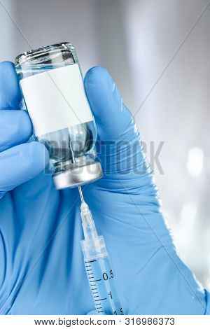 Healthcare concept with a hand in blue medical gloves holding a vaccine vial with blue liquid and blank white label