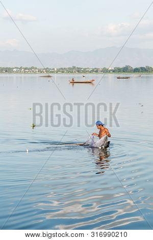 Mandalay, Myanmar - 03 December, 2018: Vertical Picture Of Local Burmese Fisherman Fishing With A Ne