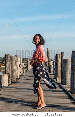 Vertical Picture Of Happy Brunette Woman Posing At Wooden U Bein Bridge, Which Is A Touristic Attrac