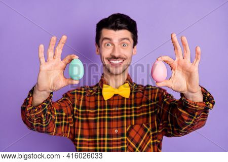 Photo Of Cute Funky Young Guy Wear Plaid Shirt Showing Pink Blue Easter Eggs Isolated Violet Color B