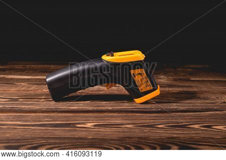 Yellow-black Pyrometer On A Wooden Background. A Device For Non-contact Temperature Measurement. Stu