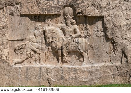 Murals Of Necropolis, King Burial Site Of Ancient Persia. King On His Horse Carved Into Sandstone Ro