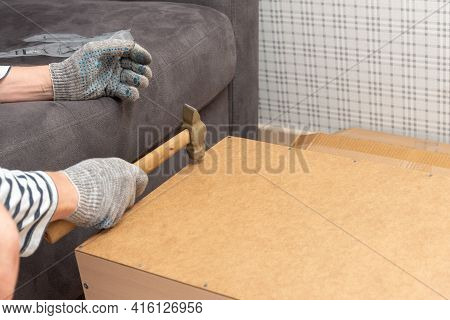 Male Hands In Gloves Hold A Hammer And Hammer In A Nail. Home Furniture Assembly, Home Office Booksh