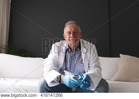 Caucasian senior male doctor holding notebook listening during consultation video call. telemedicine online during quarantine lockdown.