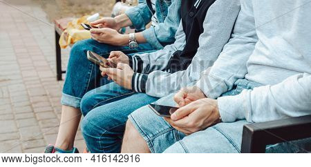 People Use A Smartphone While Sitting On A Bench In The Park