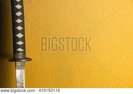 Closeup Of Japanese Sword Katana Isolated On Yellow Background Wall. Sword Used For Martial Arts Suc