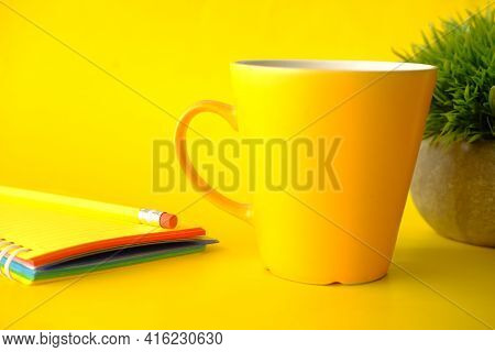 Yellow Color Coffee Mug, Pencil And Clock On Yellow Background Close Up