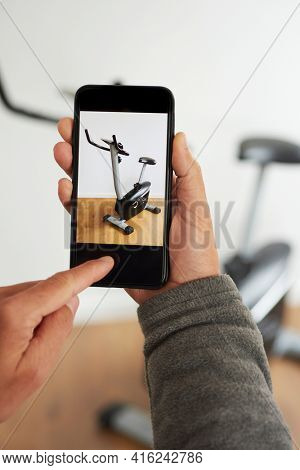 a young caucasian man takes a picture, with his smartphone, of a stationary bicycle to sell it on an online marketplace app to sell and buy secondhand goods