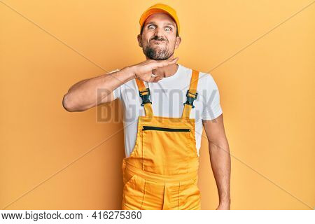 Young handsome man wearing handyman uniform over yellow background cutting throat with hand as knife, threaten aggression with furious violence 