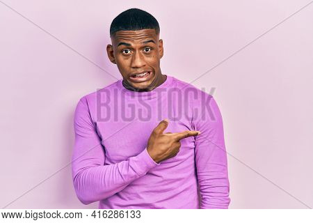 Young black man wearing casual pink sweater pointing aside worried and nervous with forefinger, concerned and surprised expression 