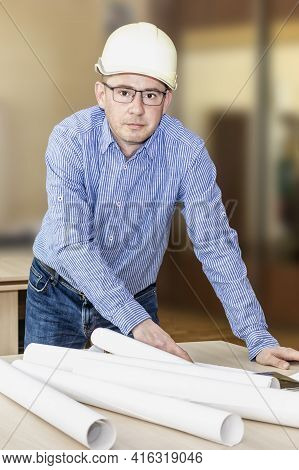 An Engineer With Glasses And A Construction Helmet Bent Over The Table With Documents. Making Change
