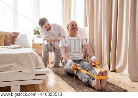 Male Yoga Trainer Helps To Senior Man To Do Asana Correctly.