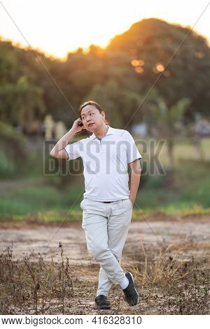 Asian Man Long Hair Stands And Relax On The Dry Field In Golden Twilight Time.