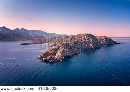 Aerial View Of Boat Passing Revellata Lighthouse In The Evening Sun On A Rocky Promontory Near Calvi
