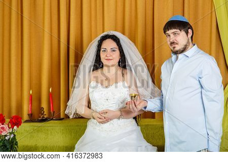During The Chuppah Ceremony In The Synagogue, The Groom Holds A Glass Of Wine In His Hand, The Bride