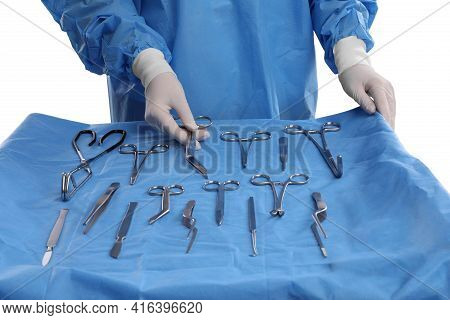 Doctor Holding Pott's Scissors Near Table With Different Surgical Instruments On Light Background, C