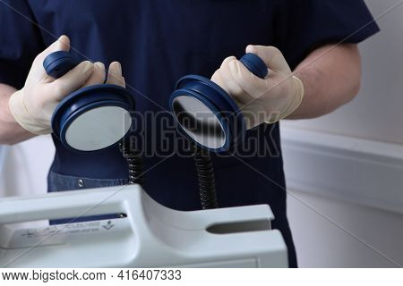 Preparing For Defibrillation. The Resuscitator Holds Electrodes In His Hands To Restore The Heart Rh