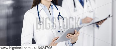 Unknown Woman Doctor Iusing Tablet Computer In Her Hands, While Standing In Clinic. Medicine Concept