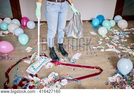 Woman With Pushbroom Cleaning Mess Of Floor In Room After Party Confetti