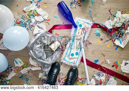 Woman With Pushbroom Cleaning Mess Of Floor In Room After Party Confetti