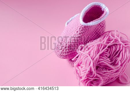 Skein Of Pink Yarn With Crochet And Knitted Shoes On A Colored Background Needlework On The Backgrou