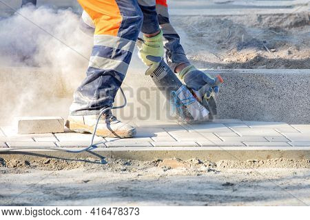A Builder Cuts Paving Slabs With An Electric Grinder And Diamond Cutting Disc, Creating A Cloud Of D
