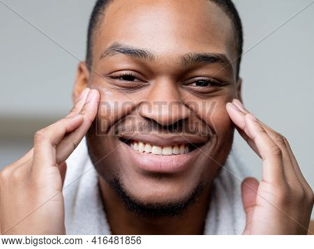 Man Skincare. Anti Aging Cosmetology. Grooming Selfcare. Happy Cheerful African Guy Applying Face Cr