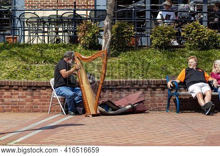 Frederick, Md, Usa 04-07-2021: An Elderly Caucasian Busker Is Playing Harp On The Street In Carroll 