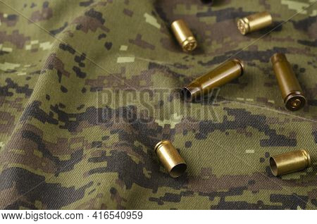 A Few Random Casings On Camouflage Cloth. A Group Of Pistol And Rifle Empty Casings Lie On Military 
