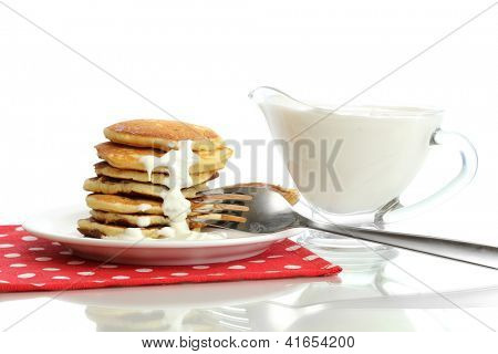 หวาน pancakes บนแผ่นกับนมข้นที่แยกต่างหากบนพื้นสีขาว