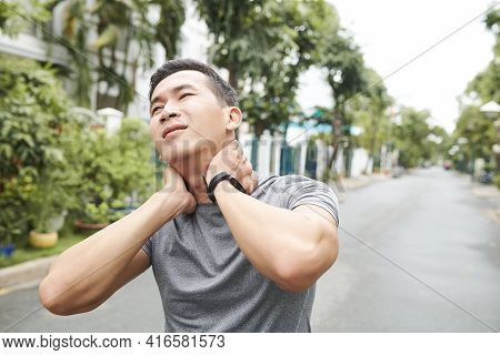 Young Asian Sportsman Suffering From Pain In His Neck, He Is Massaging Neck To Get Relief