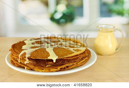 หวาน pancakes บนแผ่นกับนมข้นบนโต๊ะในห้องครัว