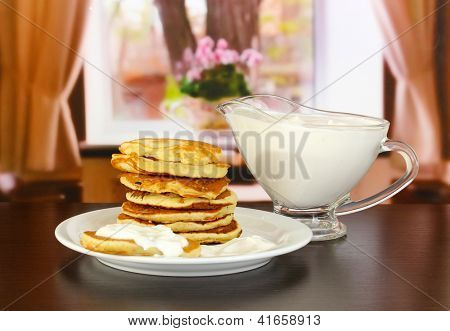 หวาน pancakes บนแผ่น ด้วยครีมเปรี้ยวบนโต๊ะในห้อง