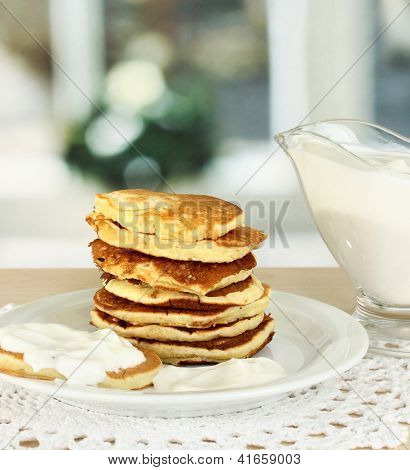 หวาน pancakes บนแผ่น ด้วยครีมเปรี้ยวบนโต๊ะในห้องครัว