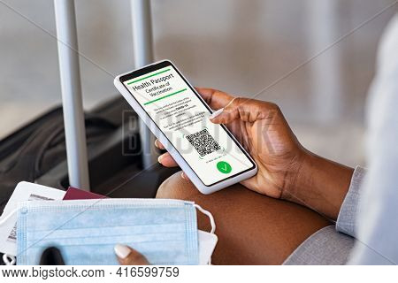 Businesswoman displaying health passport for covid-19 while traveling during coronavirus pandemic. Close up of black hands of woman in airport checking her valid digital vaccination passport for covid